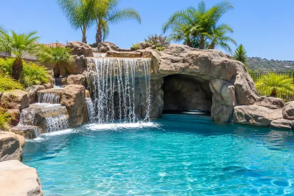 Artificial rock waterfall and grotto beside a turquoise backyard pool